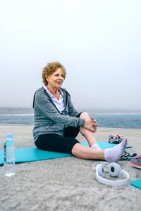 Young woman sitting on beach against clear sky