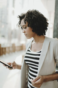 Woman using mobile phone while standing by window at cafe