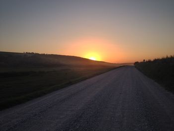 Road amidst land against clear sky during sunset