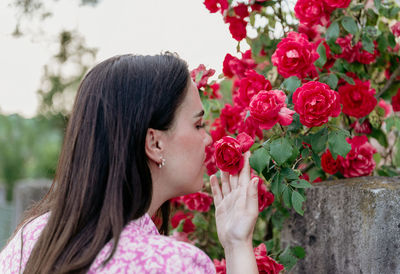 Close-up photo of young woman smelling red roses in spring