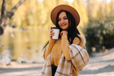 Beautiful smiling girl in casual clothes drinking coffee walking in nature in autumn outdoor