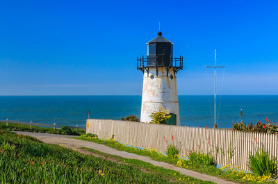 Lighthouse by sea against clear blue sky