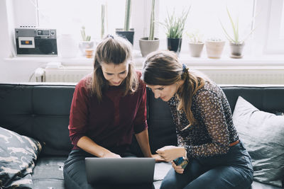 High angle view of female colleagues discussing over laptop while sitting in creative office