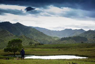 Young man standing on field against pond and mountains