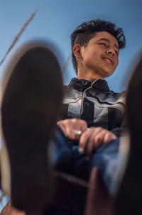 Low angle view of smiling young man sitting against sky