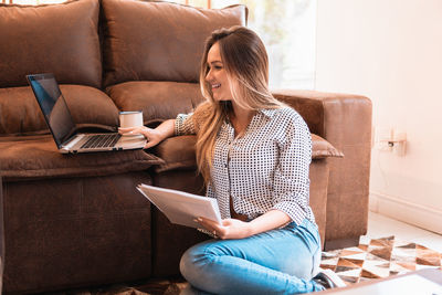 Young woman using laptop while sitting on sofa at home