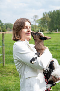Young woman plays with goat kids, feeding them, sun shining, countryside