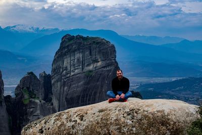 Man sitting on rock by mountains against sky