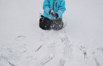 Low section of boy kneeling on snow field during winter