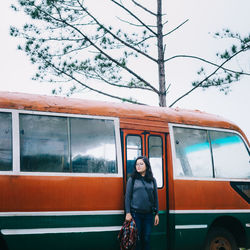 Portrait of woman standing by car against sky