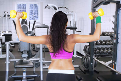 Rear view of woman lifting dumbbells in gym