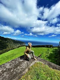 Woman sitting on grass against sky