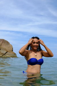 Young woman in bikini standing on rock against sea