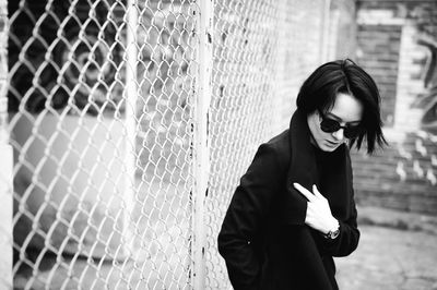 Young woman in sunglasses standing against chainlink fence