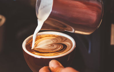 Cropped hand of person pouring milk in coffee cup