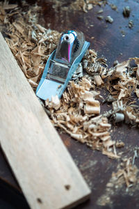 High angle view of spokeshave and wooden planks surrounded by wood curls on table.