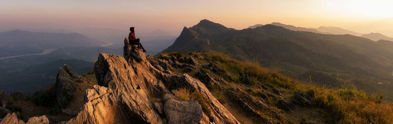 Person sitting on mountain against sky during sunset