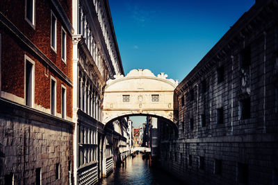 Bridge of sighs amidst buildings over canal against blue sky