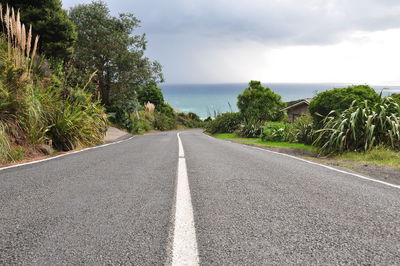 Empty road by sea against cloudy sky