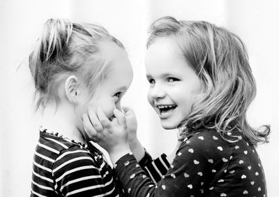 Close-up portrait of cheerful girl with sister by wall