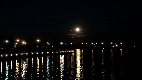 Illuminated street lights by river against sky at night