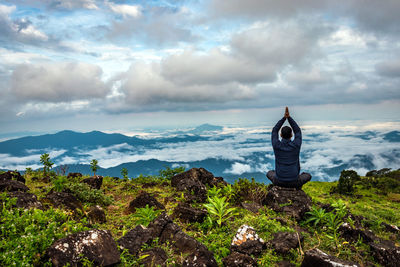 Rear view of man doing meditation on rock with pristine mountain with dramatic sky view