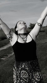 Woman with arms raised standing on field against sky