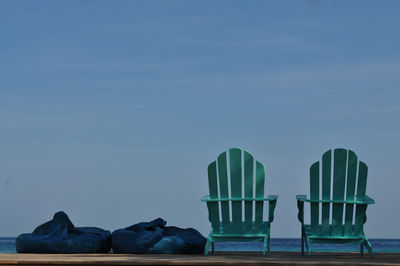 Adirondack chairs with bean bags on pier against sky