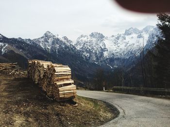 Stack of logs on snow covered mountain against sky