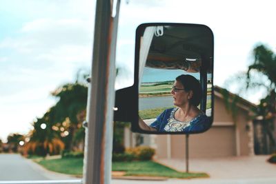 Woman reflecting on side-view mirror against sky