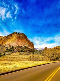 Road leading towards mountains against blue sky