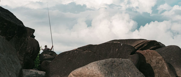 Panoramic view of man sitting on rock against sky