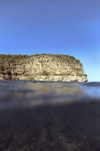 Rough cliff with green plants located near rippling clean sea