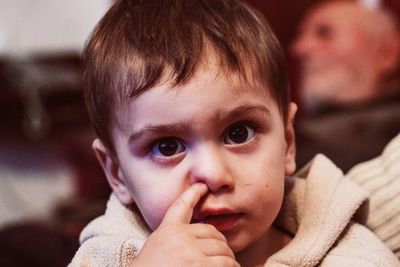 Close-up portrait of cute boy picking nose at home