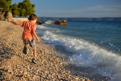 Rear view of boy on beach against sky