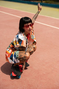 Caucasian girl with tattoos and short black hair on a sports court skating with a skateboard