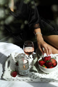 Midsection of strawberry holding ice cream on table with glass of rose wine