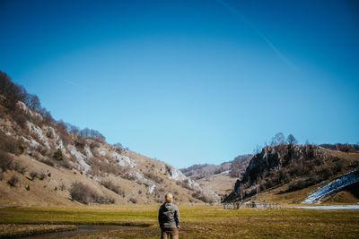 Rear view of man standing on field against clear blue sky