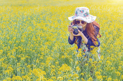 Woman photographing with camera at rape field