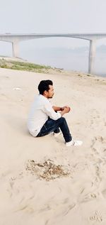 Side view of young man sitting on beach