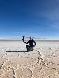 Digital composite image of woman holding man while kneeling on salt flat against blue sky