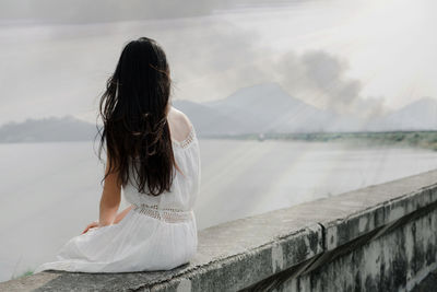 Woman sitting on retaining wall against sky