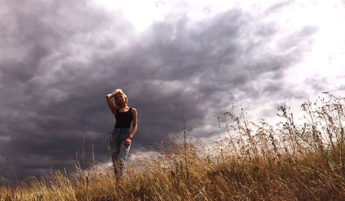 Low angle view of woman standing on field against cloudy sky