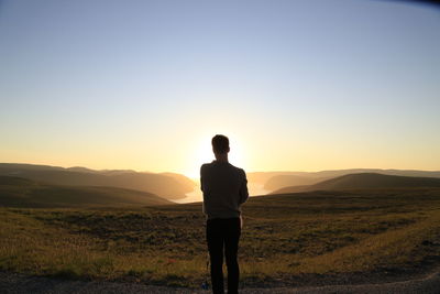 Rear view of man standing on field against sky during sunset