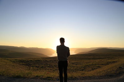 Rear view of man standing on field against sky during sunset