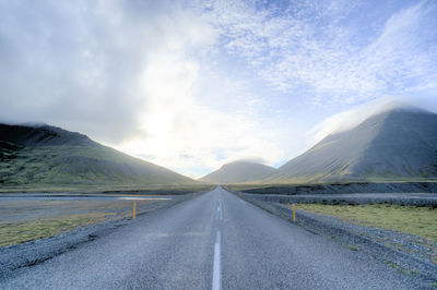 Empty road leading towards mountains against cloudy sky