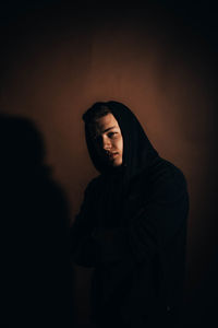 Portrait of young man wearing hooded jacket standing against brown background