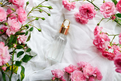 Bottle with rose essential oil and flowers on white cotton background