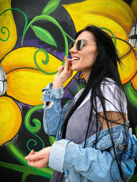 Beautiful young woman wearing sunglasses against wall