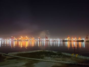 Illuminated city by sea against sky at night